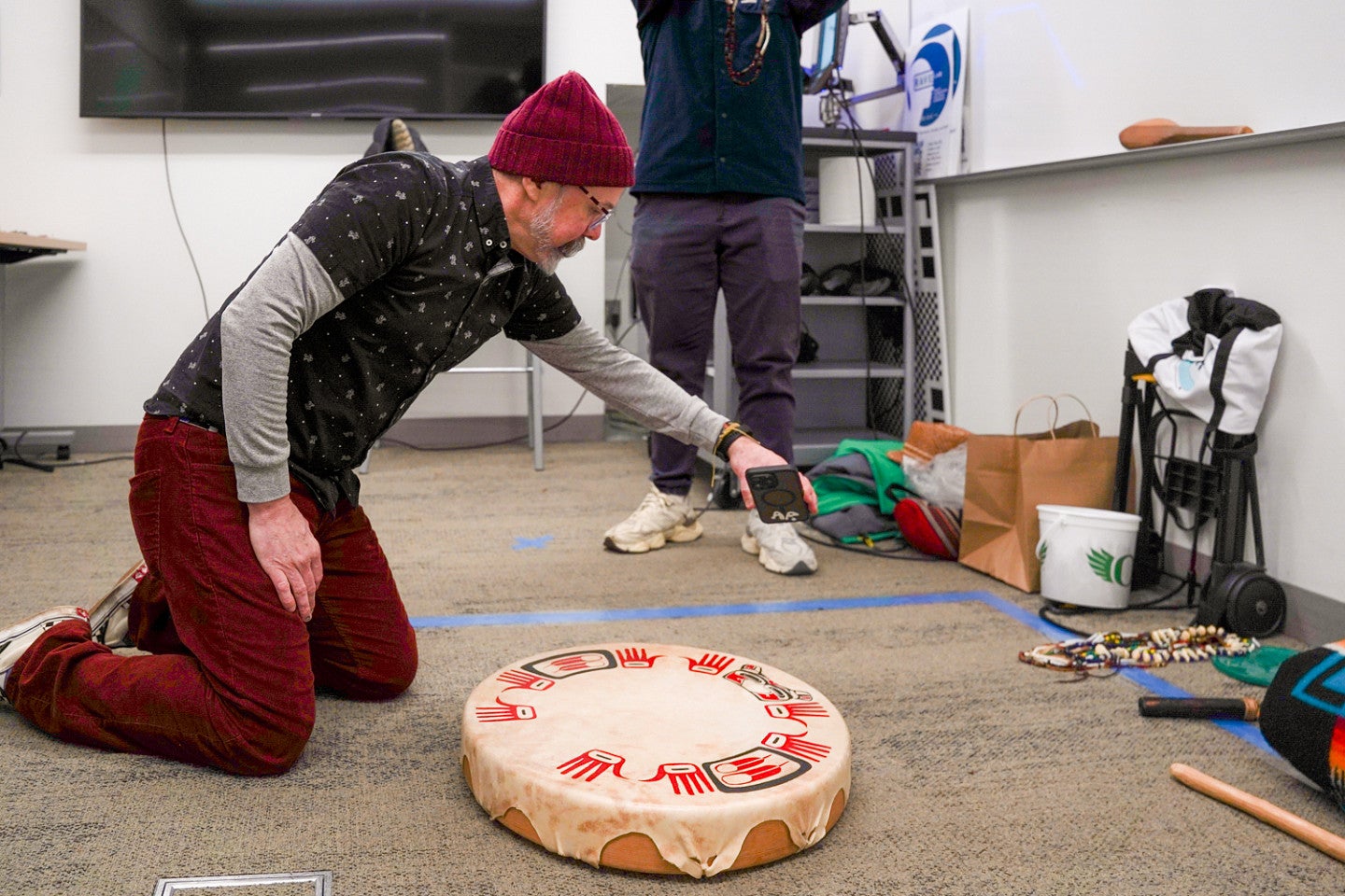 a person kneels over a traditional drum head from the Coquille Tribe and scans it using a cell phone