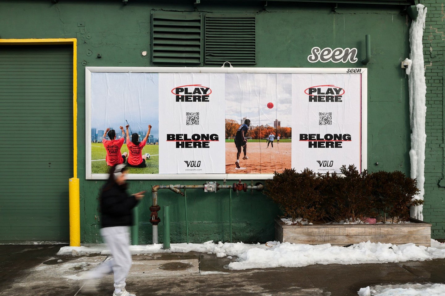 Volo Sports posters on the side of a building show photos of people playing sports with the tagline "Play Here, Belong Here."