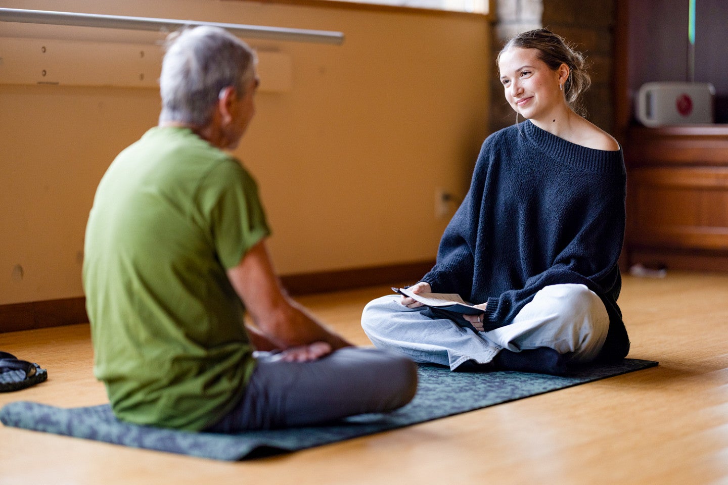 two people sit facing each other on opposite ends of a yoga mat
