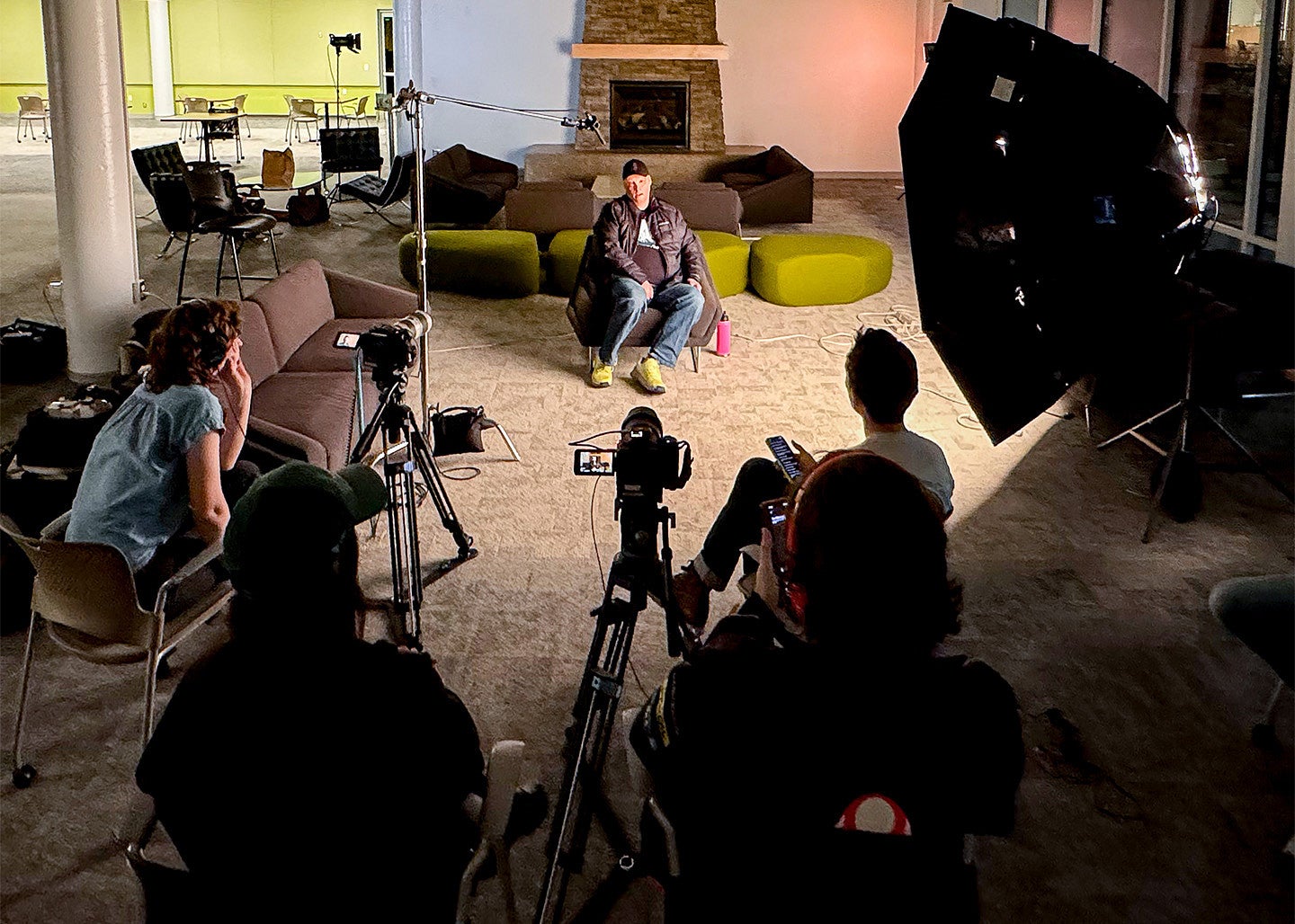 Multimedia Storytelling graduate students film a documentary interview with a subject in a dark room with professional studio lighting