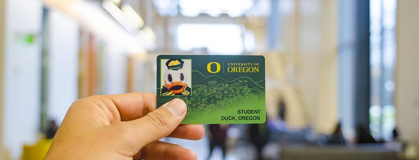 a hand holds up an example of the University of Oregon ID card