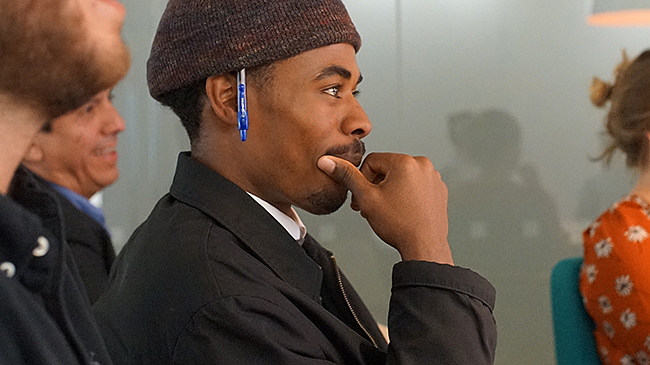 side profile view of student wearing a knit beanie with a pen tucked behind their ear