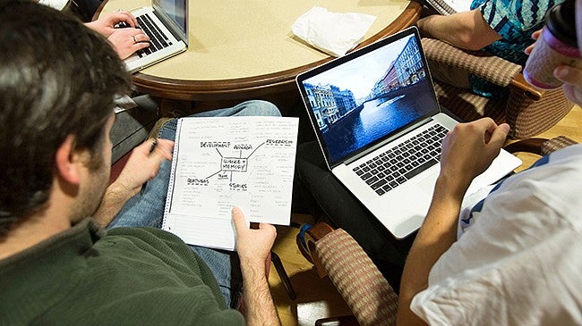 Students working on a laptop and writing in a notebook