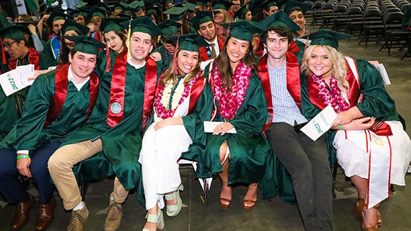students in green graduation caps and gowns at the SOJC's 2022 Commencement ceremony