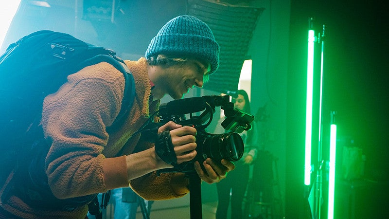 a person looks through the viewfinder of a video camera in a studio lit with green lights