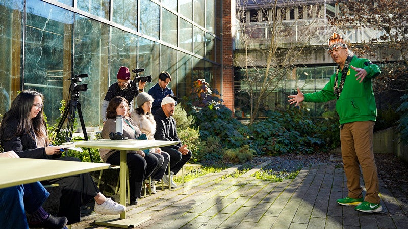 a group of people watch Jason Younker act out one of the stories of the Coquille Tribe in an outdoor courtyard