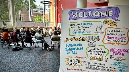 people sit in a circle of chairs with a colorful hand-drawn poster in the foreground