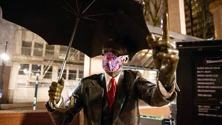 A statue of a man holding an umbrella with a cloth mask placed on it