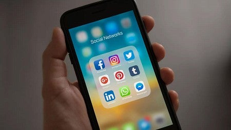 a person's hand holding a cell phone with social media app icons displayed on the screen