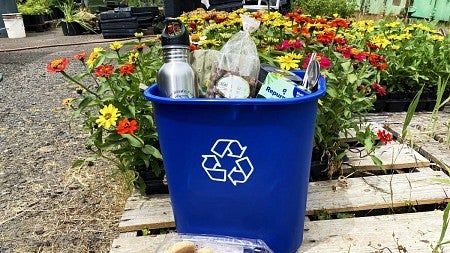 a recycling bin full of raffle prizes sits in front of colorful flowers