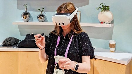 Kathleen Darby wears a VR headset in front of a wall with the Meta logo and a large screen showing an immersive environment