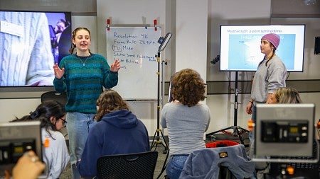 two students speak at the front of a class