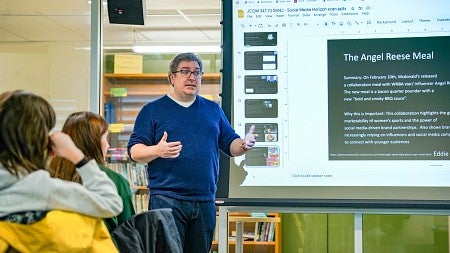 Damian Radcliffe presents next to a digital screen