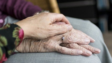 A smoother hand holds a pair of wrinkled hands