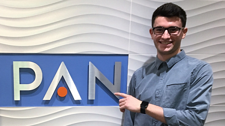 Cameron Rogers standing near PAN Communications sign.
