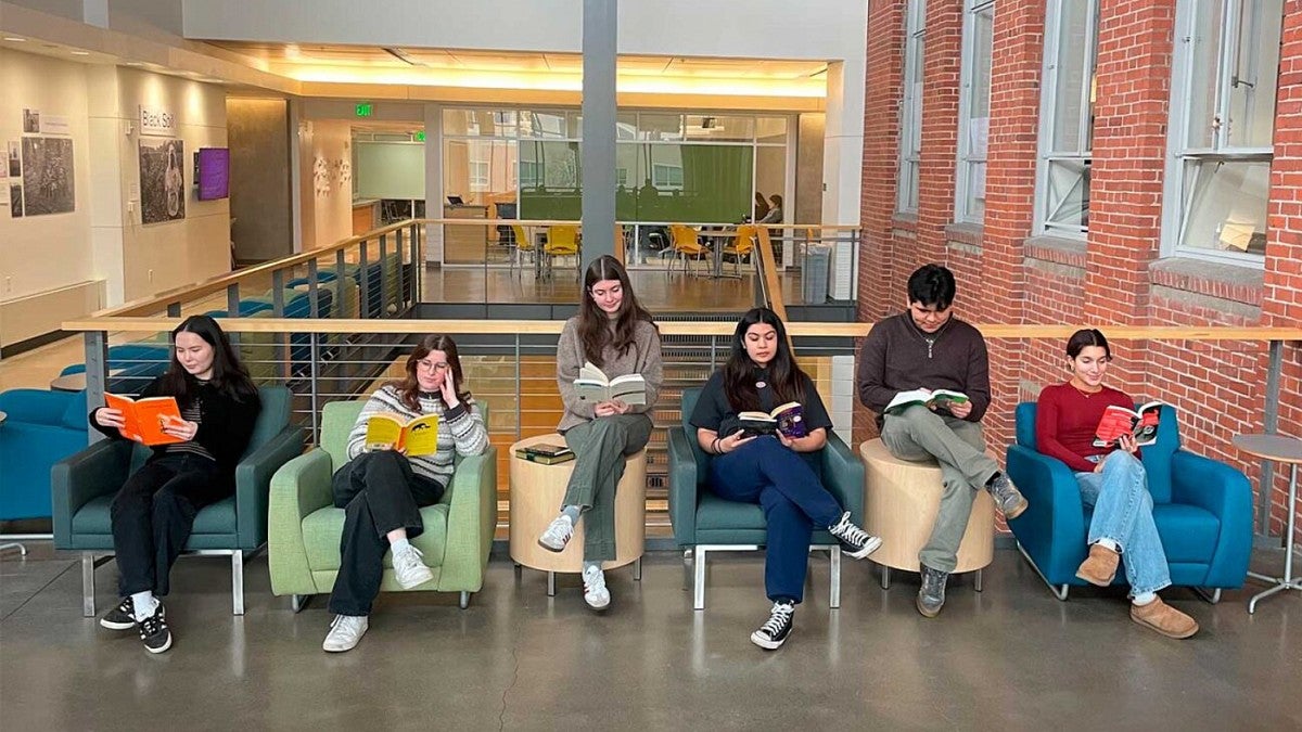 six SOJC public relations students read books while sitting in a row of chairs 