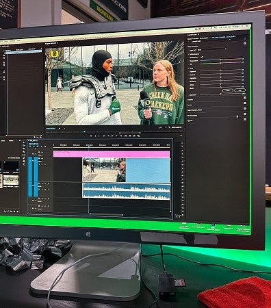 A computer monitor shows a video being edited in Adobe Premiere. The video screenshot shows Sophie Fowler holding a microphone for a student athlete wearing football pads