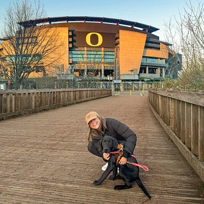 Ella Durchin poses with a black lab puppy with Autzen Stadium in the background