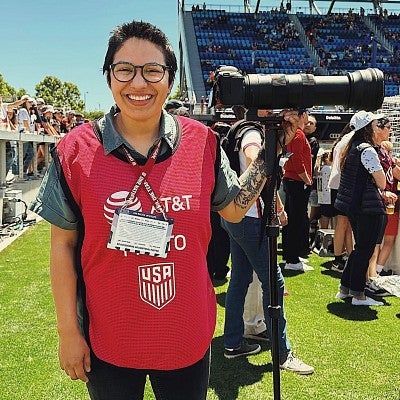 portrait of Jackie Gutierrez holding a camera at a sporting event