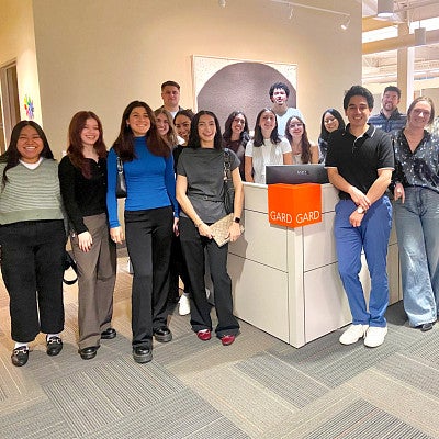 a group of students pose around a desk with an orange sign that says GARD