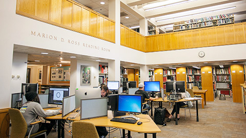 Students working in a computer lab with bookshelves along the sides of the room.