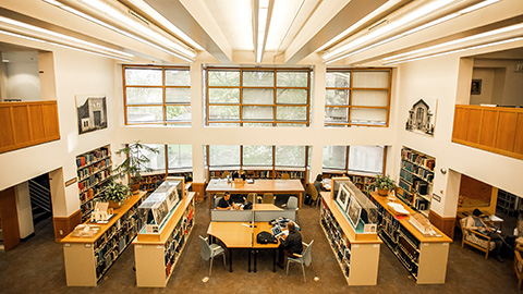 Overhead view of students working at tables surround by bookshelves and in front of large windows.