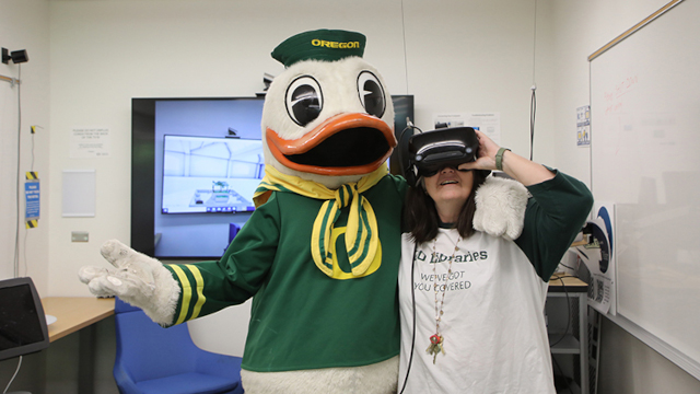 UO Mascot interacting with student using VR headset.