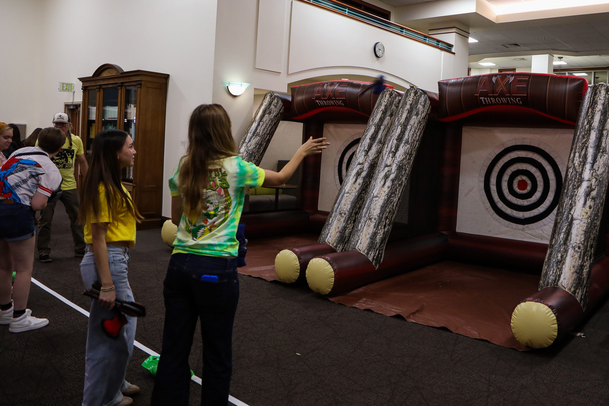 Students throwing velcro axes at targets inside two inflatable "Axe Throwing" party concessions.