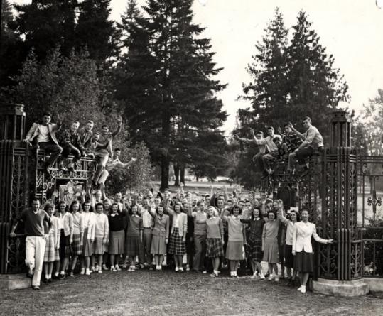View of a group of people standing and sitting in front of a iron fence.