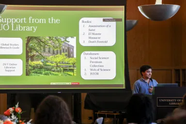 student gives presentation at a podium with a large digital screen behind them