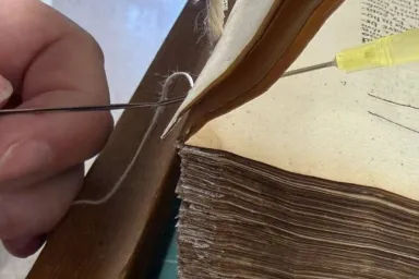Close-up image of conservator's hand rethreading a book binding using a hypodermic needle.using a 