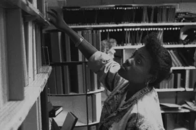 A student reaches for a book on the UO bookstore shelves, circa 1980.