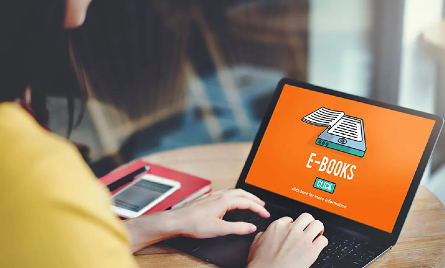 Female-presenting person types on a laptop with screen showing an image of ebook.