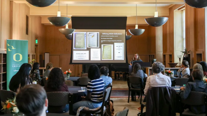 a student gives a presentation in front of a large screen while people watch