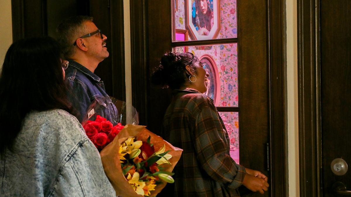 Three people looking into phone booth housing Tiny galleries exhibit; one is holding a bouquet of flowers.