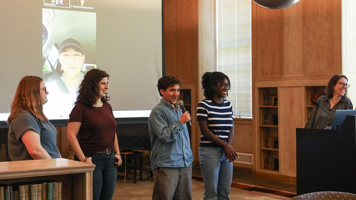 four students stand at the front of the room and answer questions