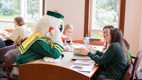 The Duck mascot at a table with students in the library