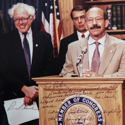 Peter DeFazio speaking at a podium, Bernie Sanders is standing to his right.