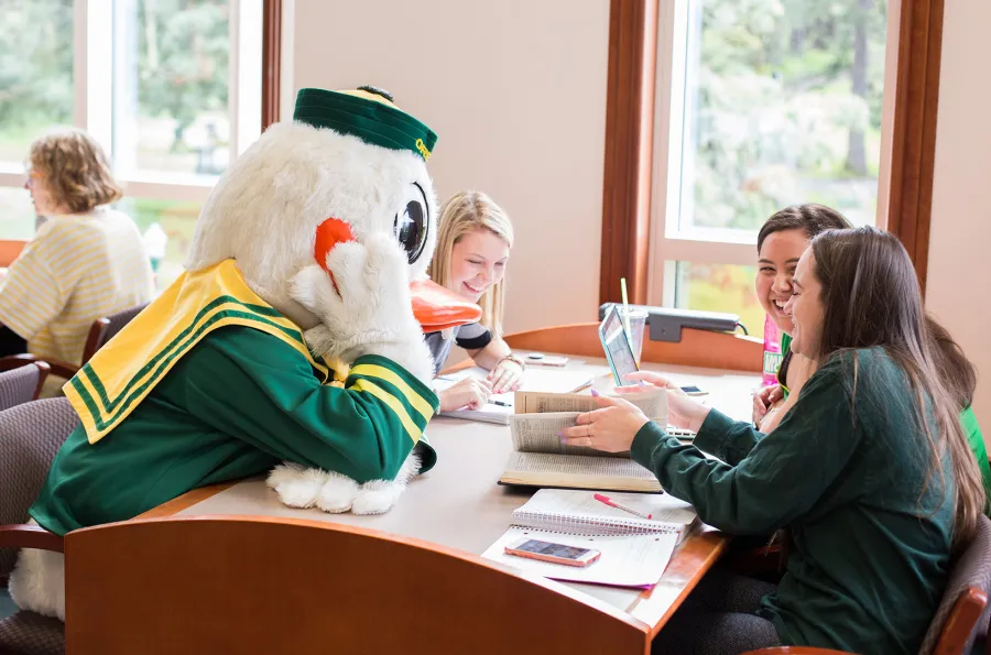 The Duck mascot at a table with students in the library
