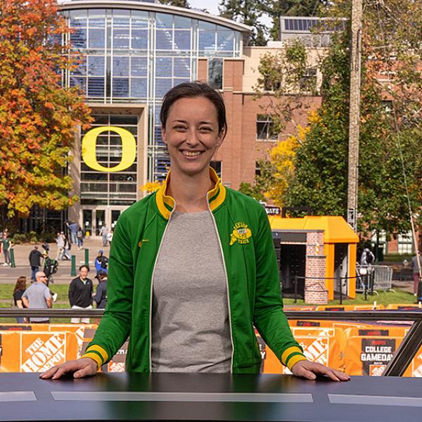 person outside at news desk with trees and buildings behind her