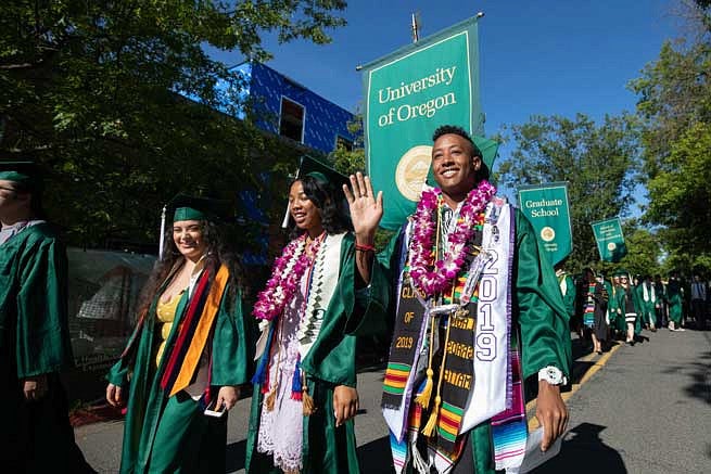 A graduate waving at the camera while walking in the Duck Grad Parade
