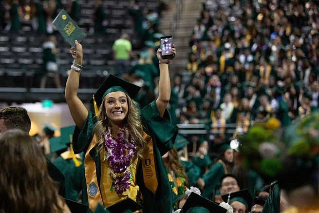 A graduate gesturing to friends and family in the stands during the commencement ceremony