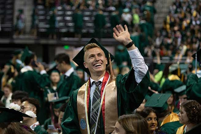 A graduate waving to the stands during the commencement ceremony