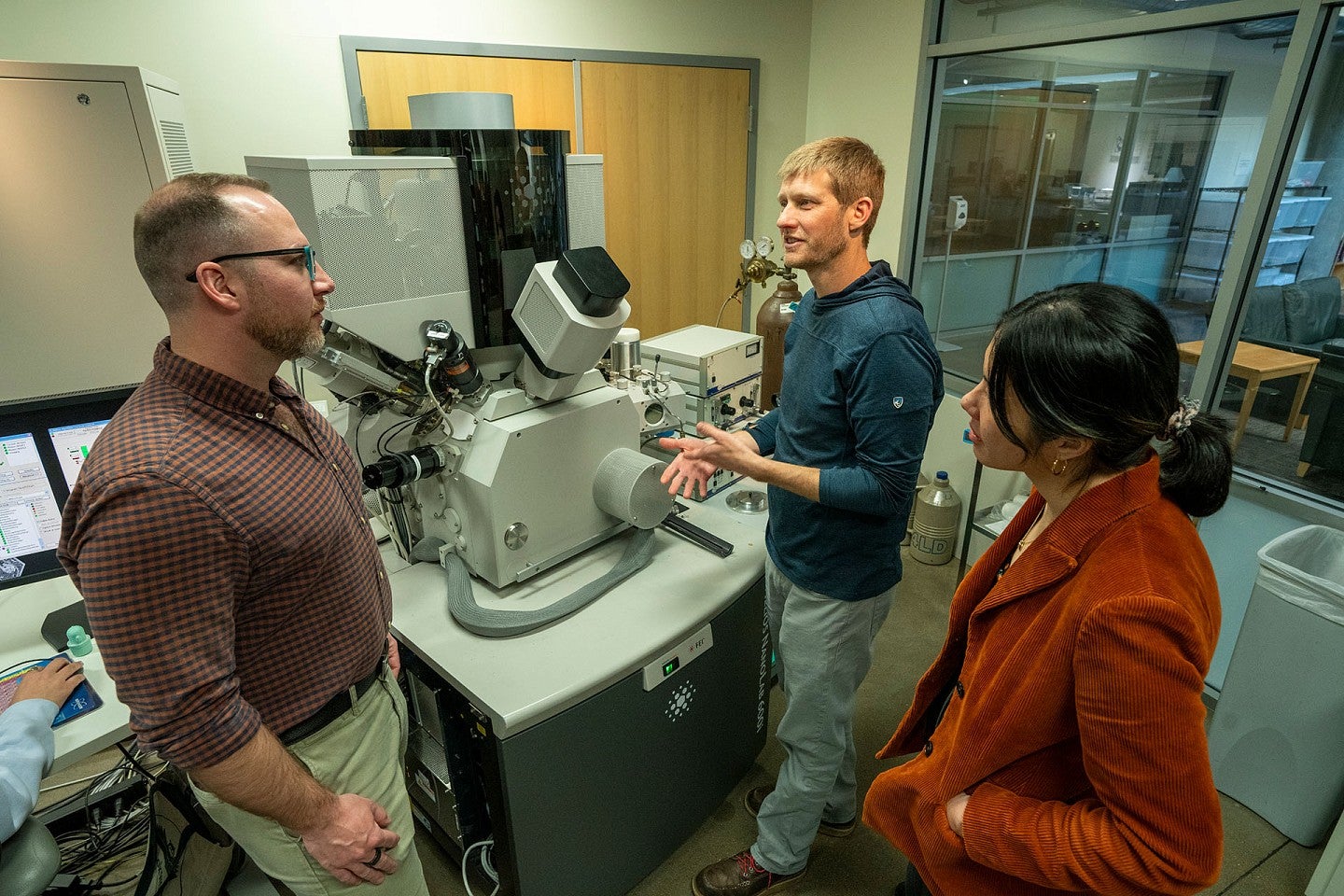 Three people around electron microscope
