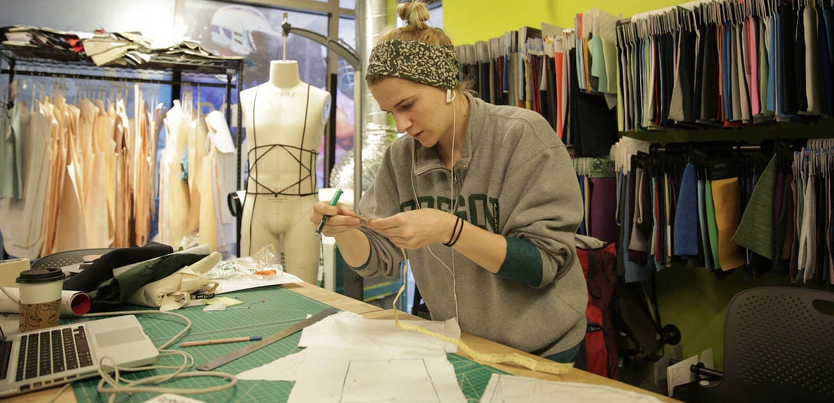 Student creating a sewing pattern in a room with fabric swatches around them