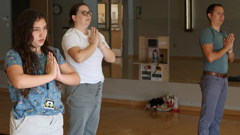 A husband, wife and daughter stand with hands clasped in a yoga studio