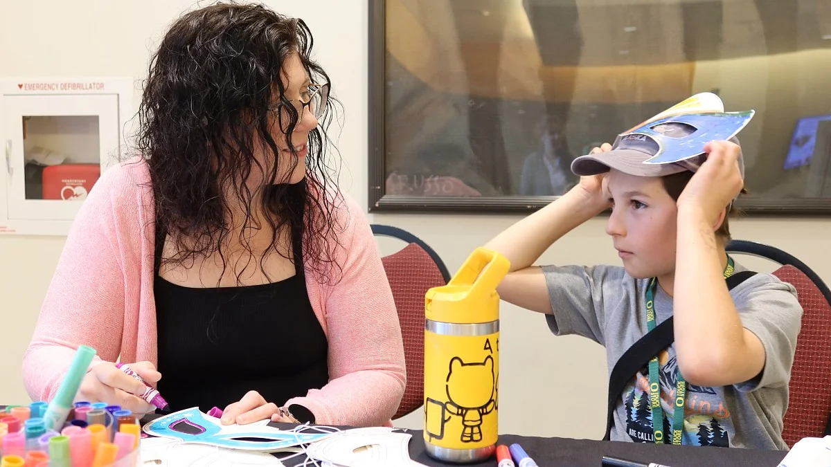 A woman smiles at a child who has a superhero mask on top of his head