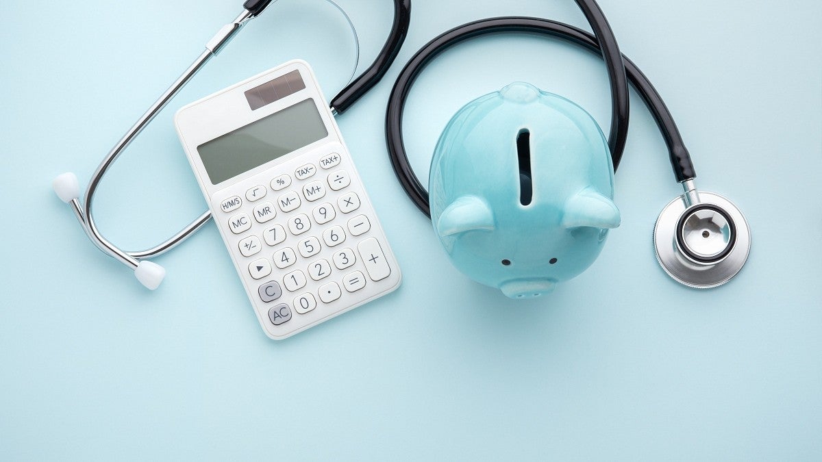 A stethoscope with a white calculator and light blue piggy bank displayed together