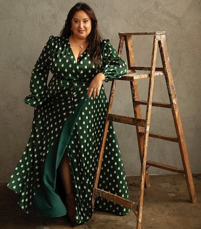 A woman in a green dress poses next to a rustic ladder