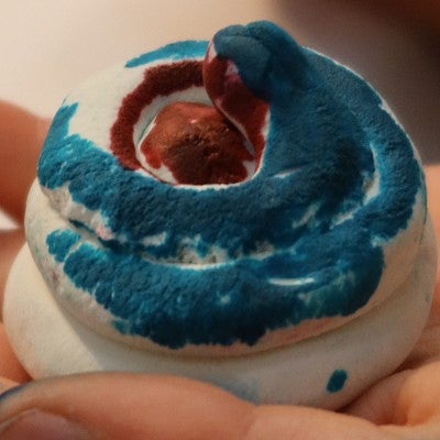 A closeup shows a clay sculpture of a coiled snake, painted green